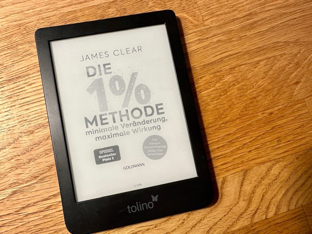 eReader mit Buch "Die 1%-Methode" von James Clear liegt auf Holztisch