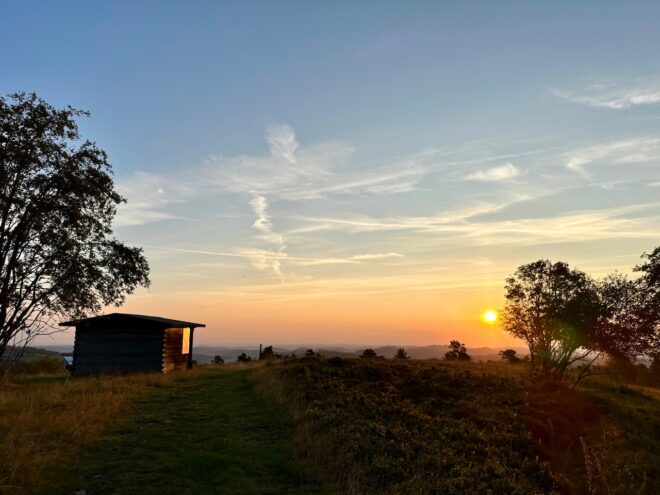 Sonnenaufgang. Im Vordergrund eine Schutzhütte und ein paar Bäume rechts und links.